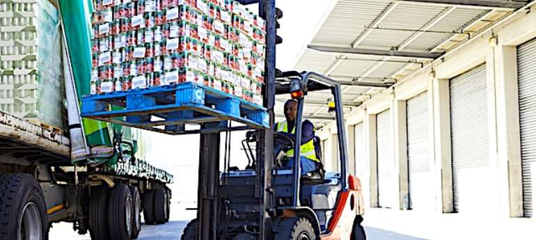 Fork lift truck loading a pallet of tinned tomatoes onto a lorry outside a large food distribution warehouse.