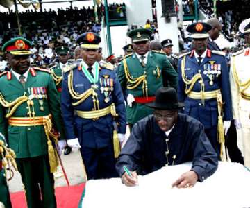 PRESIDENT GOODLUCK JONATHAN SIGNING THE ANNIVERSARY REGISTER AFTER THE PARADE. BEHIND HIM ARE SERVICE CHIEFs.<br/>